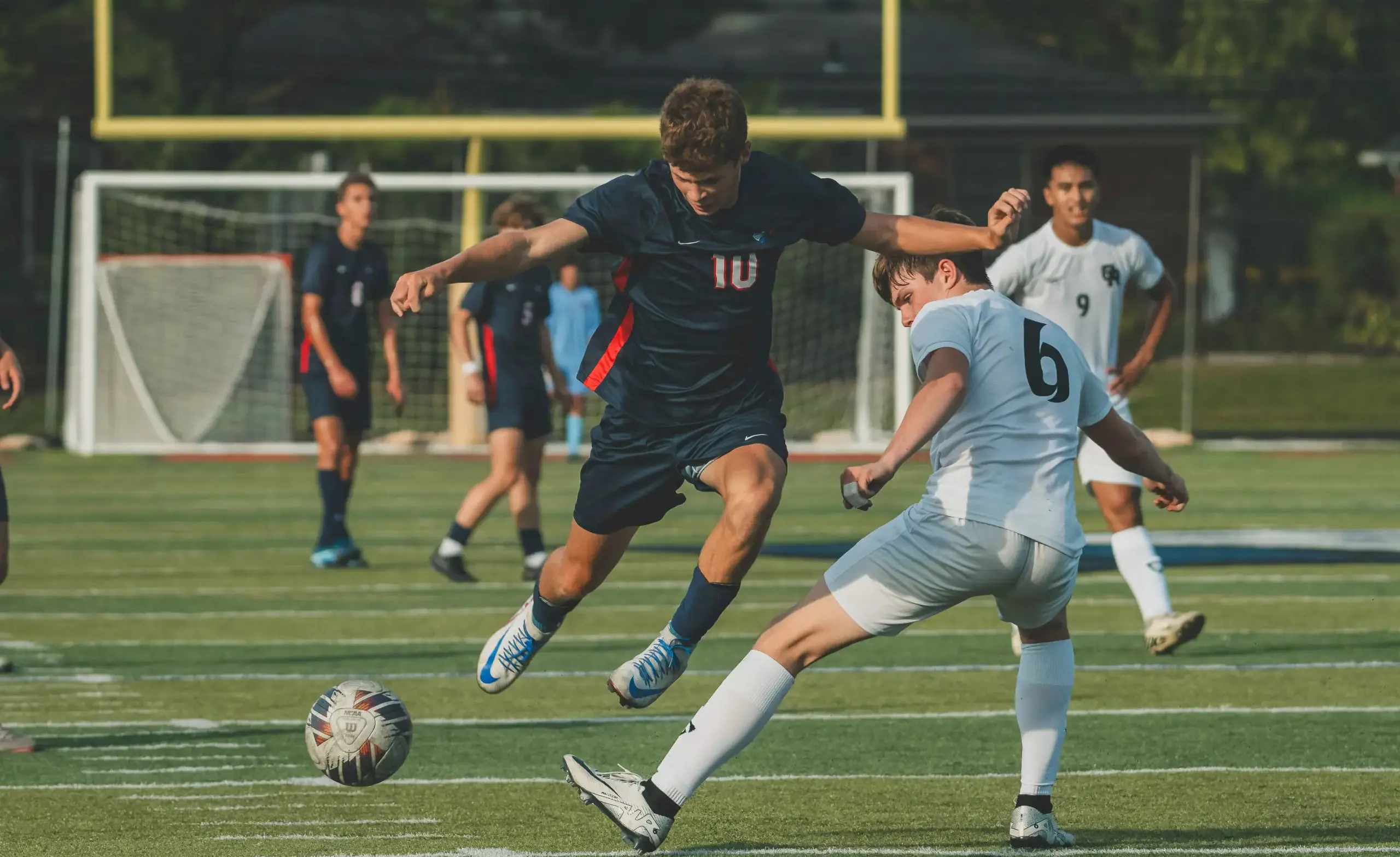Boys soccer player jumps over soccer ball during game