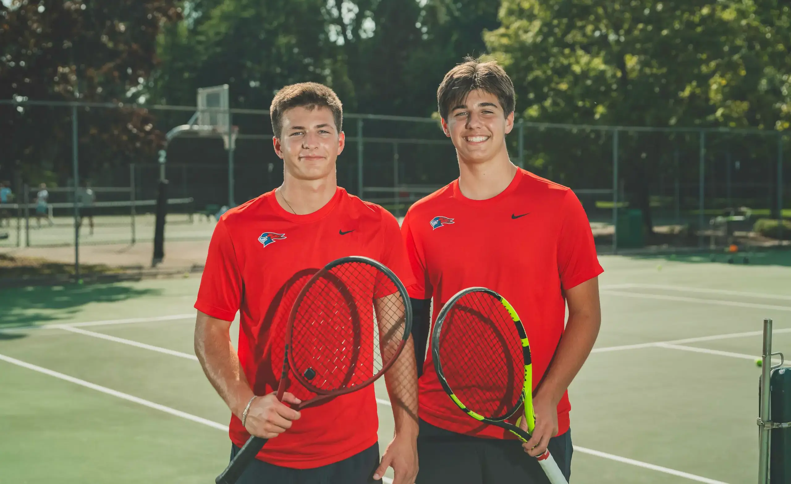 Two tennis players smile at the camera holding their rackets